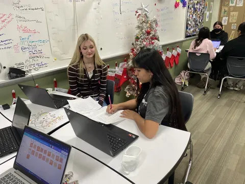 two students at a desk turn to each other in conversation
