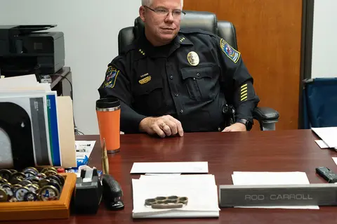 A police officer in uniform sits behind a desk.