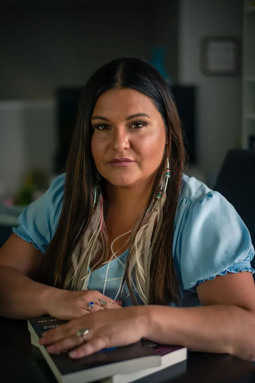 Brandi Morin portrait. Morin is sitting at a table with hands laid on a book.