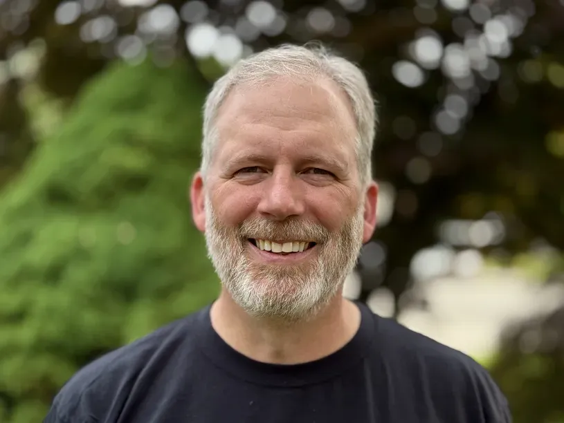 A headshot of Fred Haas. He is smiling at the camera with trees in the background.