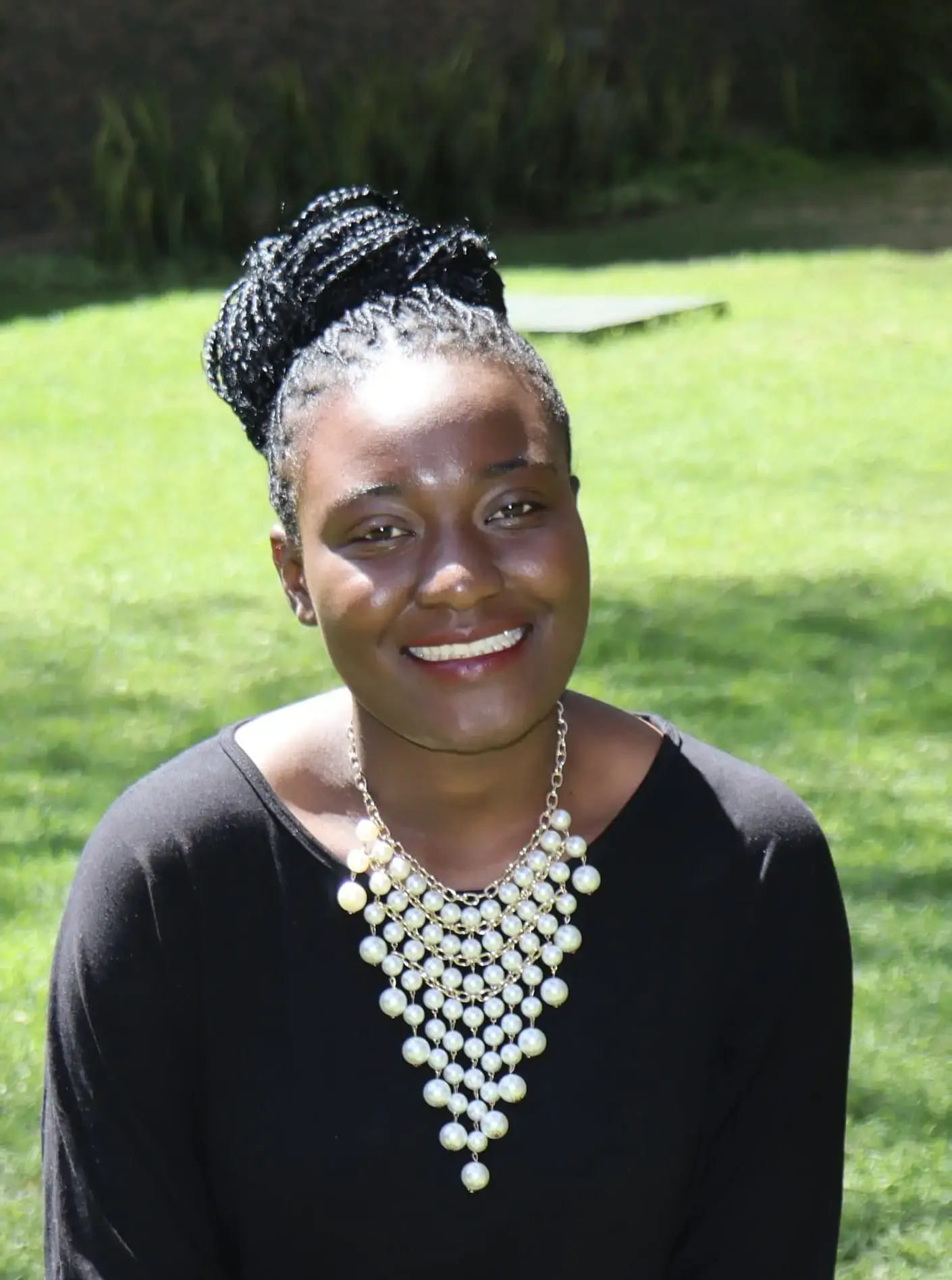 Headshot of Nelly wearing black with a white necklace in a grass field