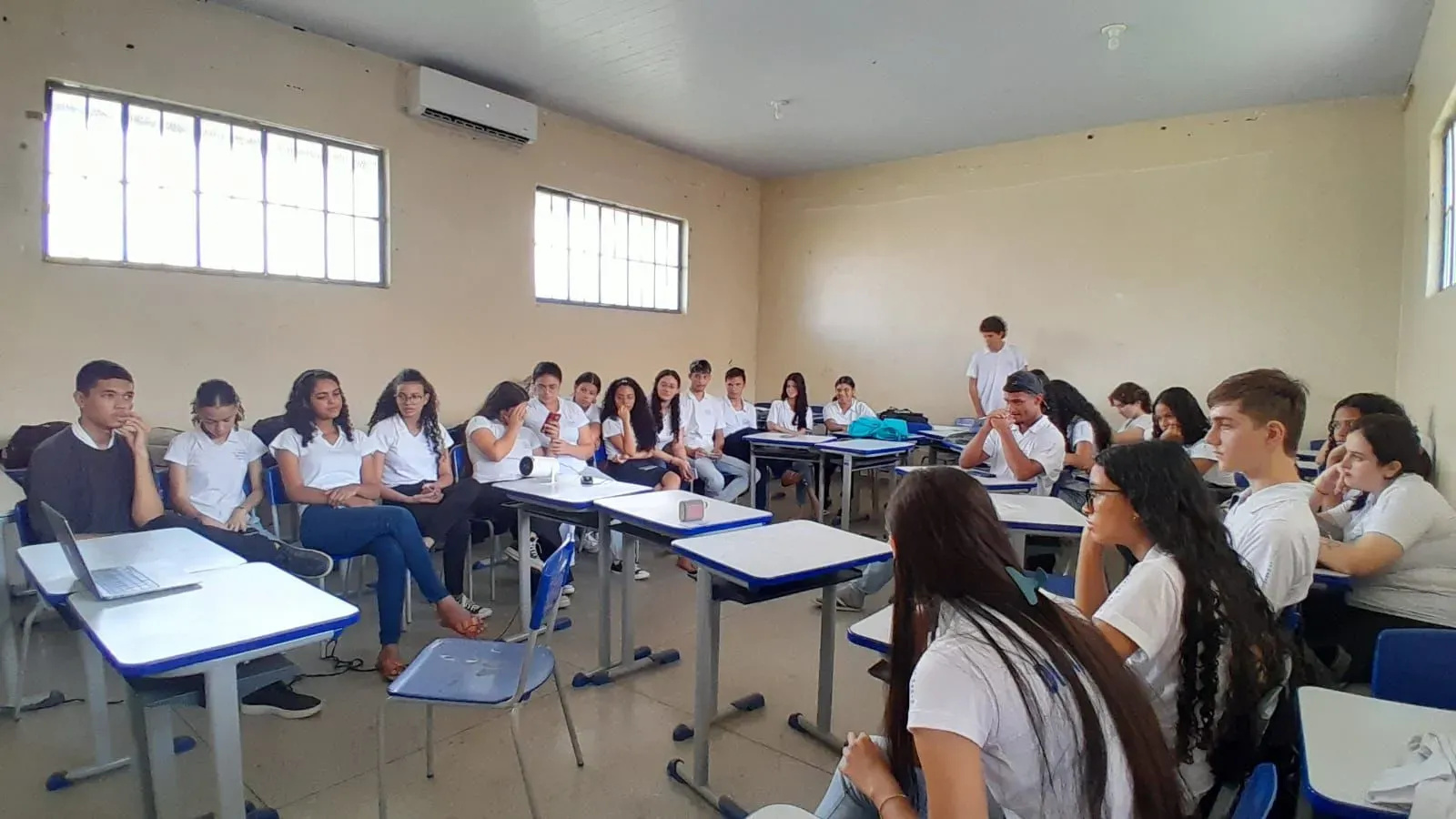 Students gather their desks into a U shape to watch content that is projecting from a laptop in a classroom