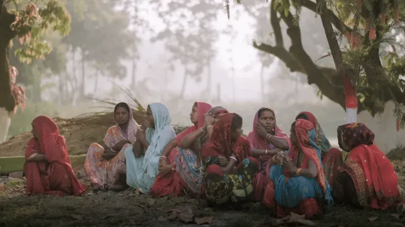 women in colorful headscarves sit in a forest clearing, India
