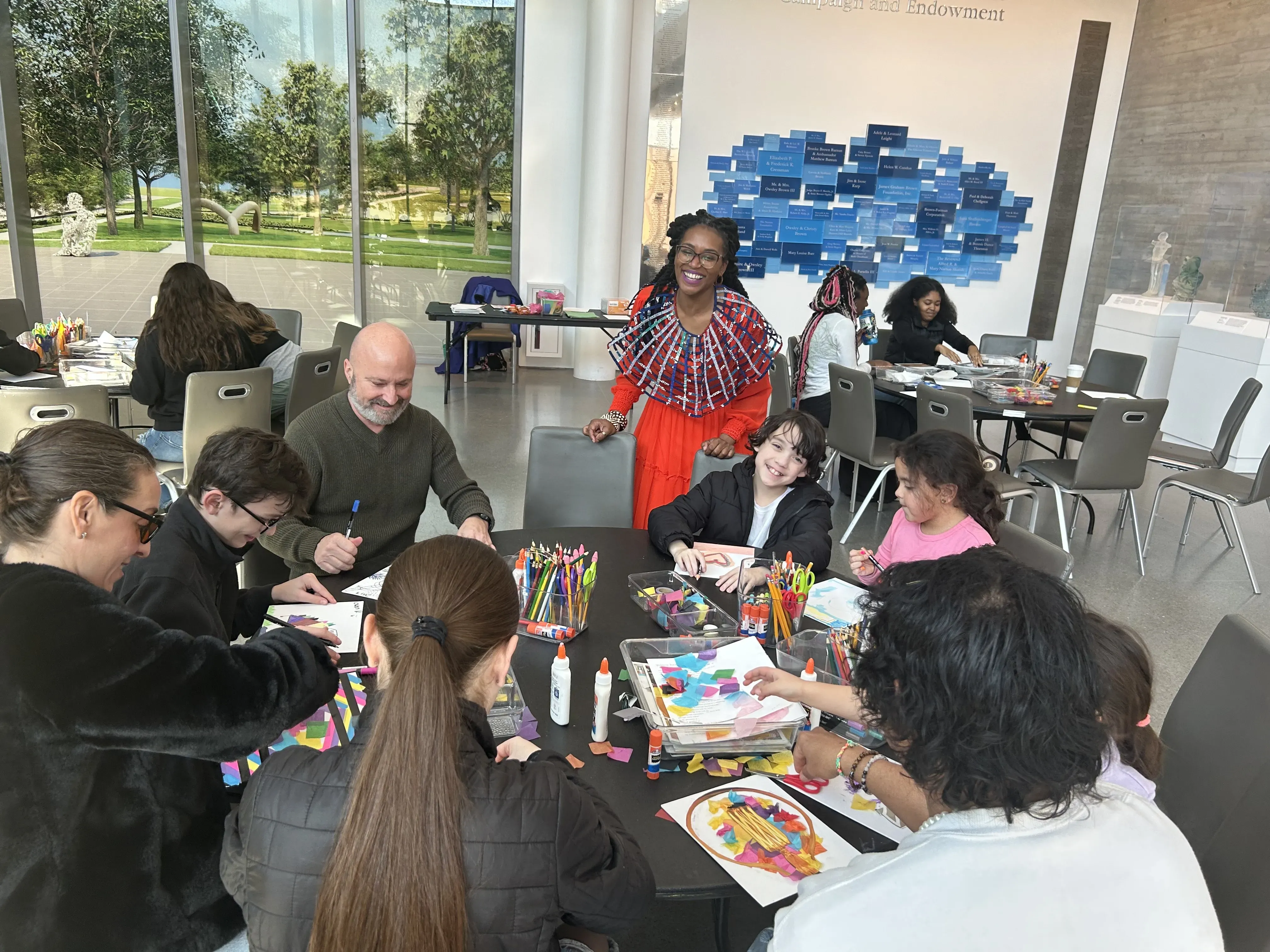 adults and children sit around a table, creating art