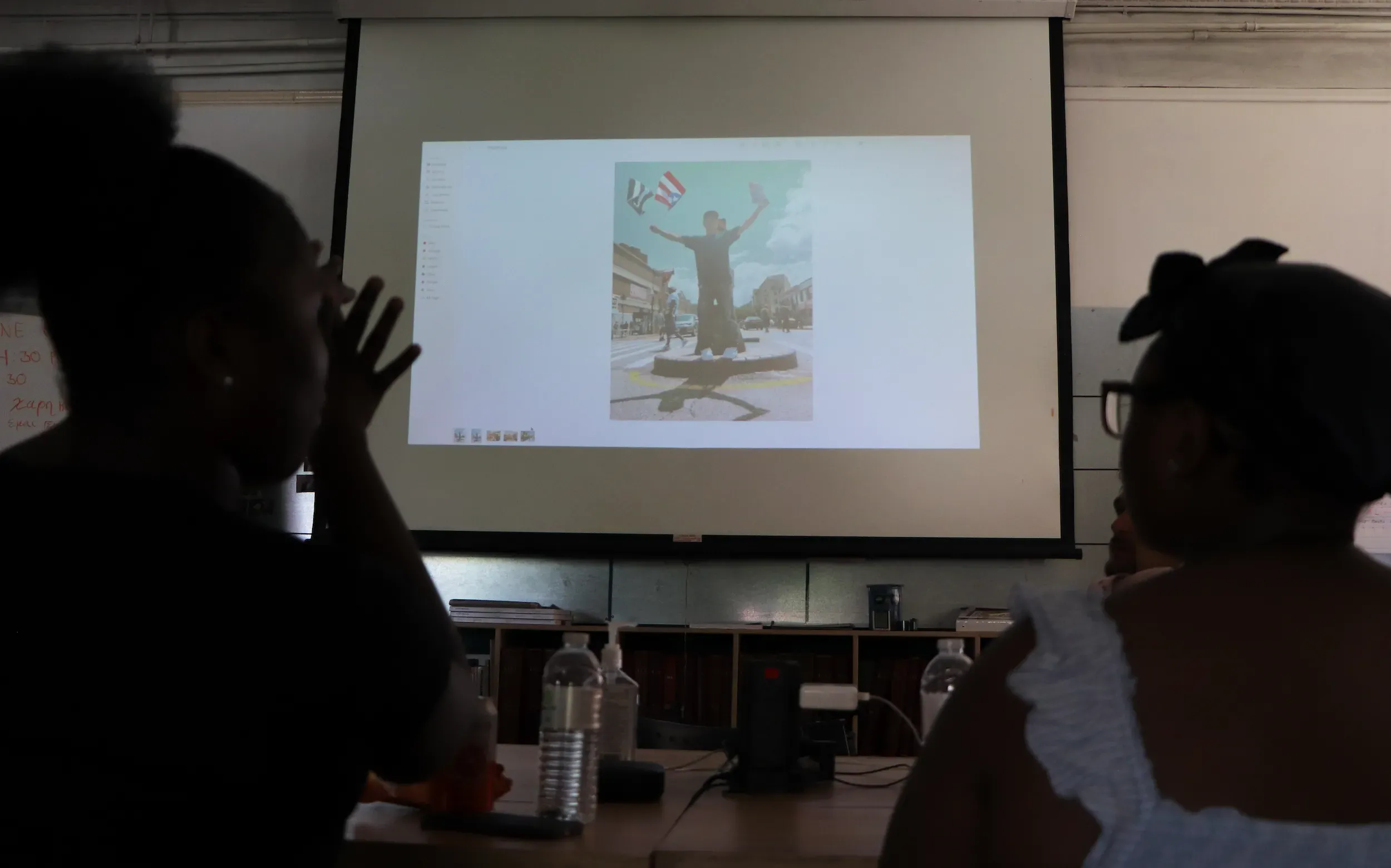 Two people discuss image in background on projector screen