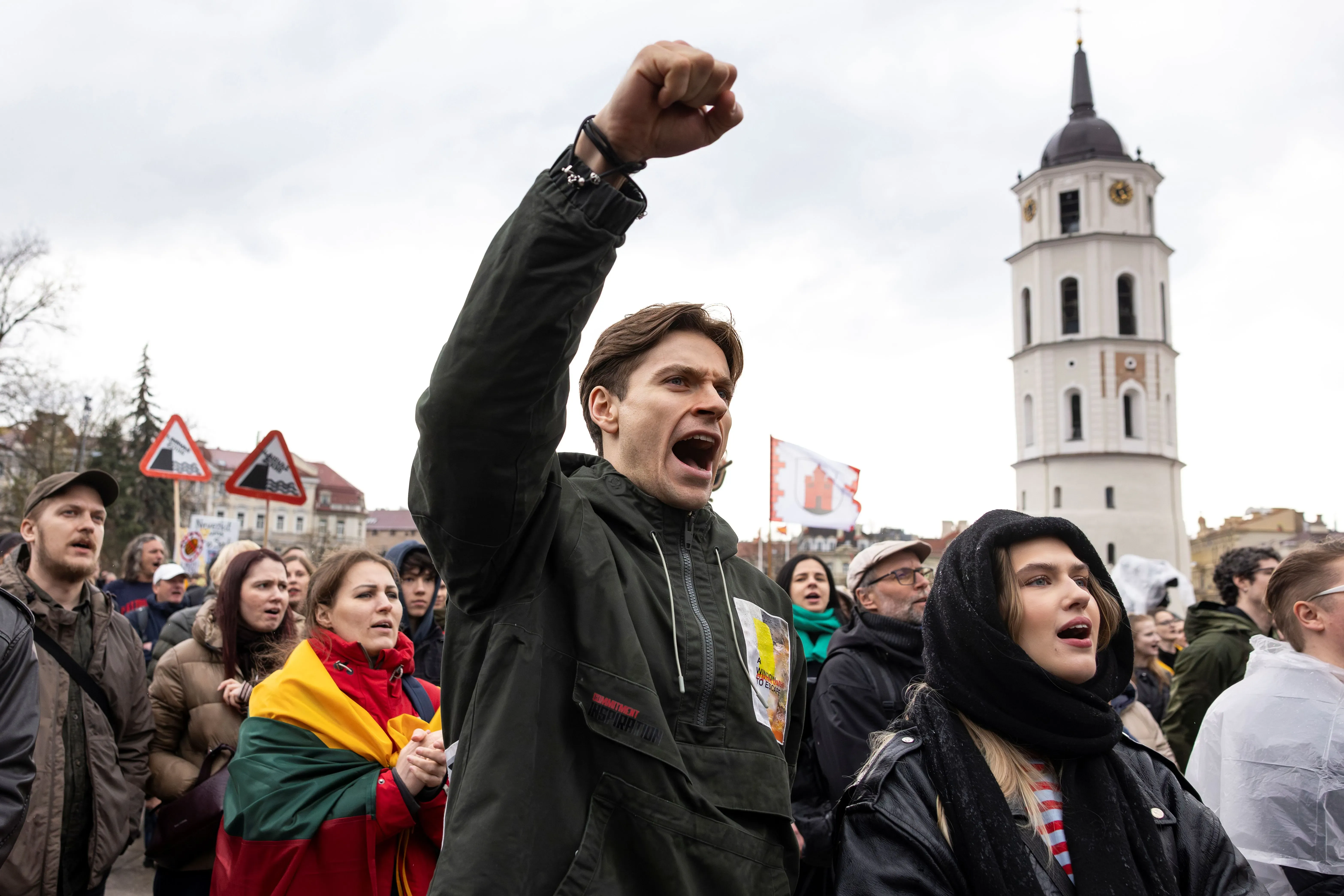 a man holds his fist high and yells in protest among others in an outdoor setting