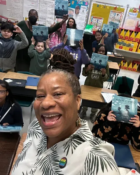 Project Lead Veronica Jones takes a selfie with a class of elementary students who hold up copies of Born on the Water
