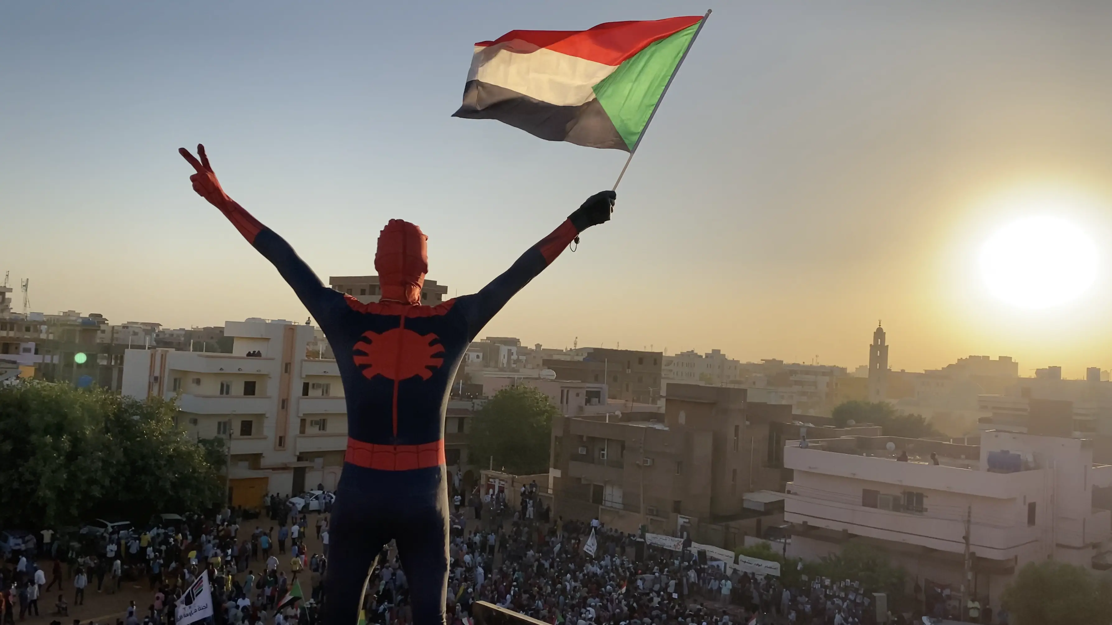 A man in a spider-man outfit stands above a protest in Sudan