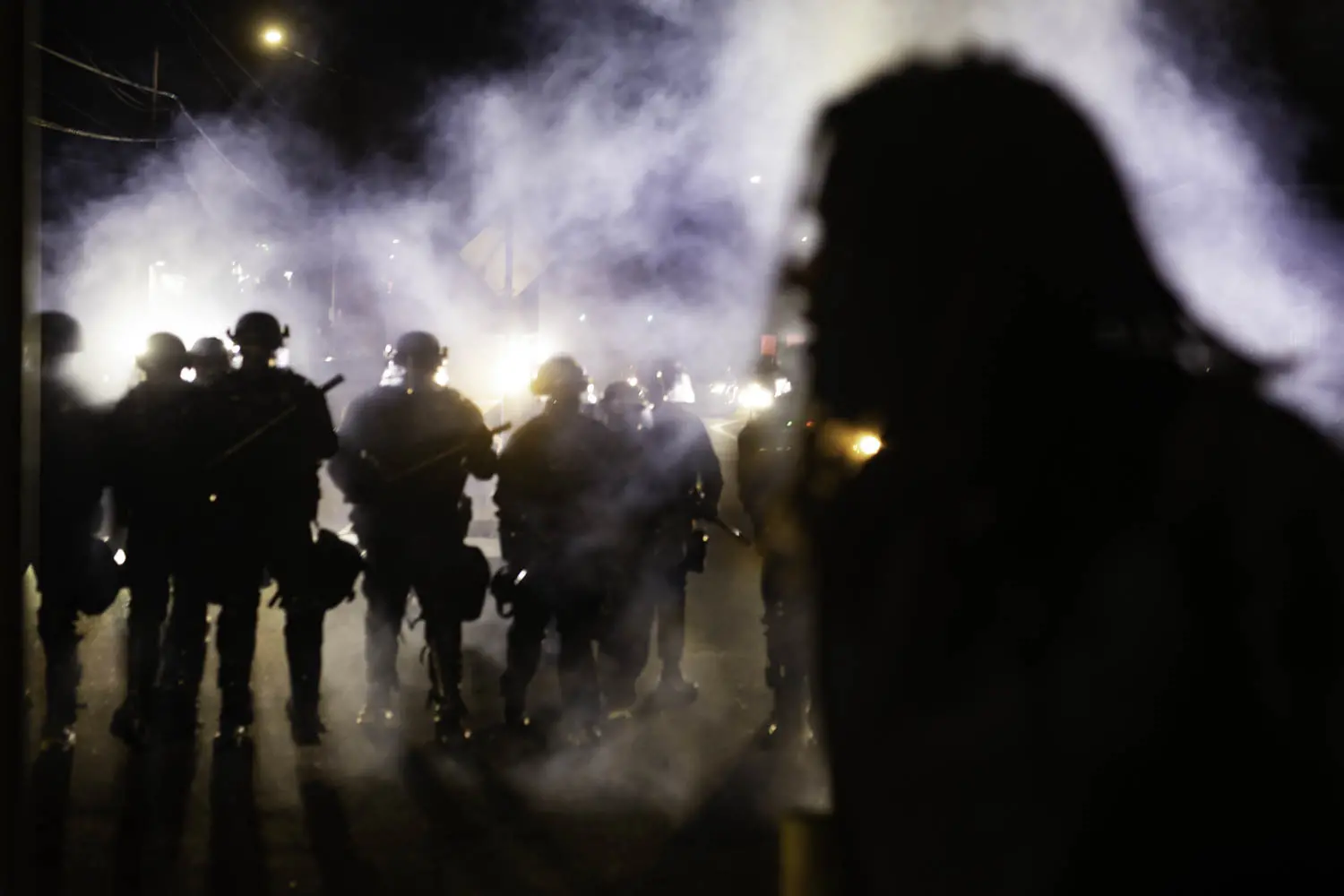 A protester crosses the street as a line of Portland police officers approach amidst a cloud of teargas on the night of August 9, 2020.