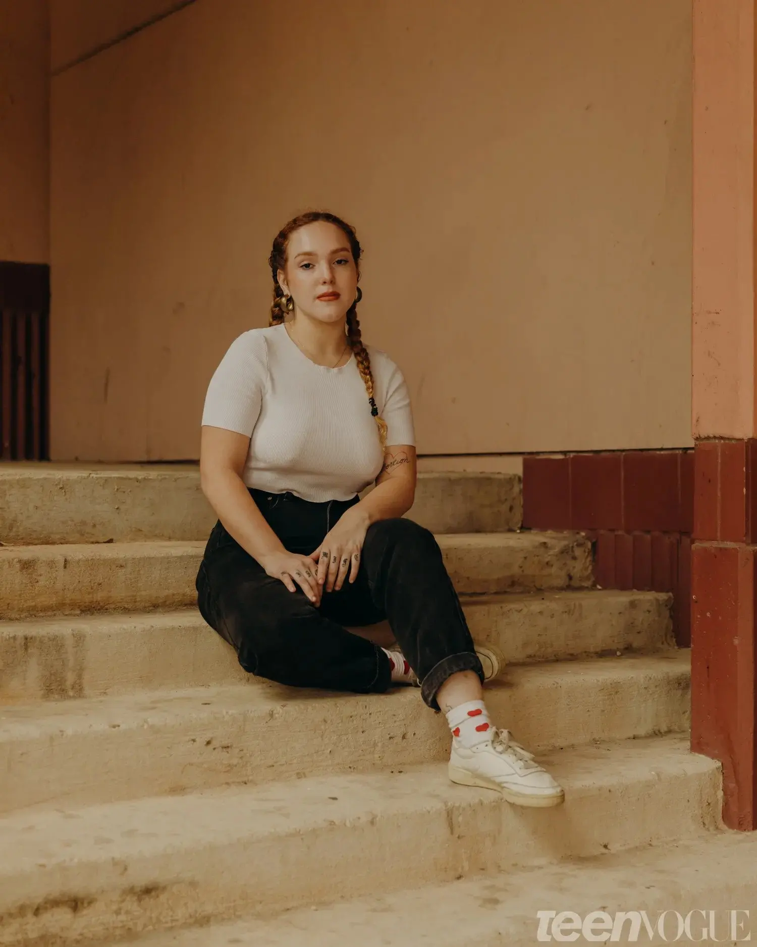 A girl in a white tee shirt and jeans sits on the steps of building.