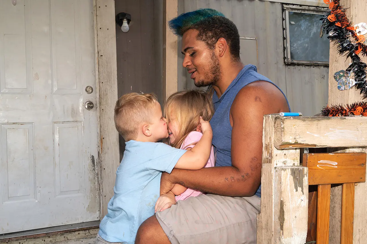 DeVon Noe sits with two children on a porch.