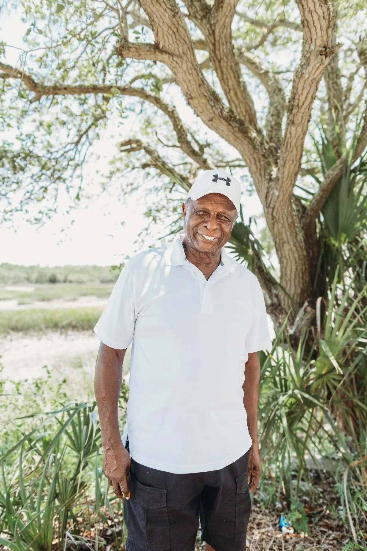 A man smiles in front of a tree on the beach.