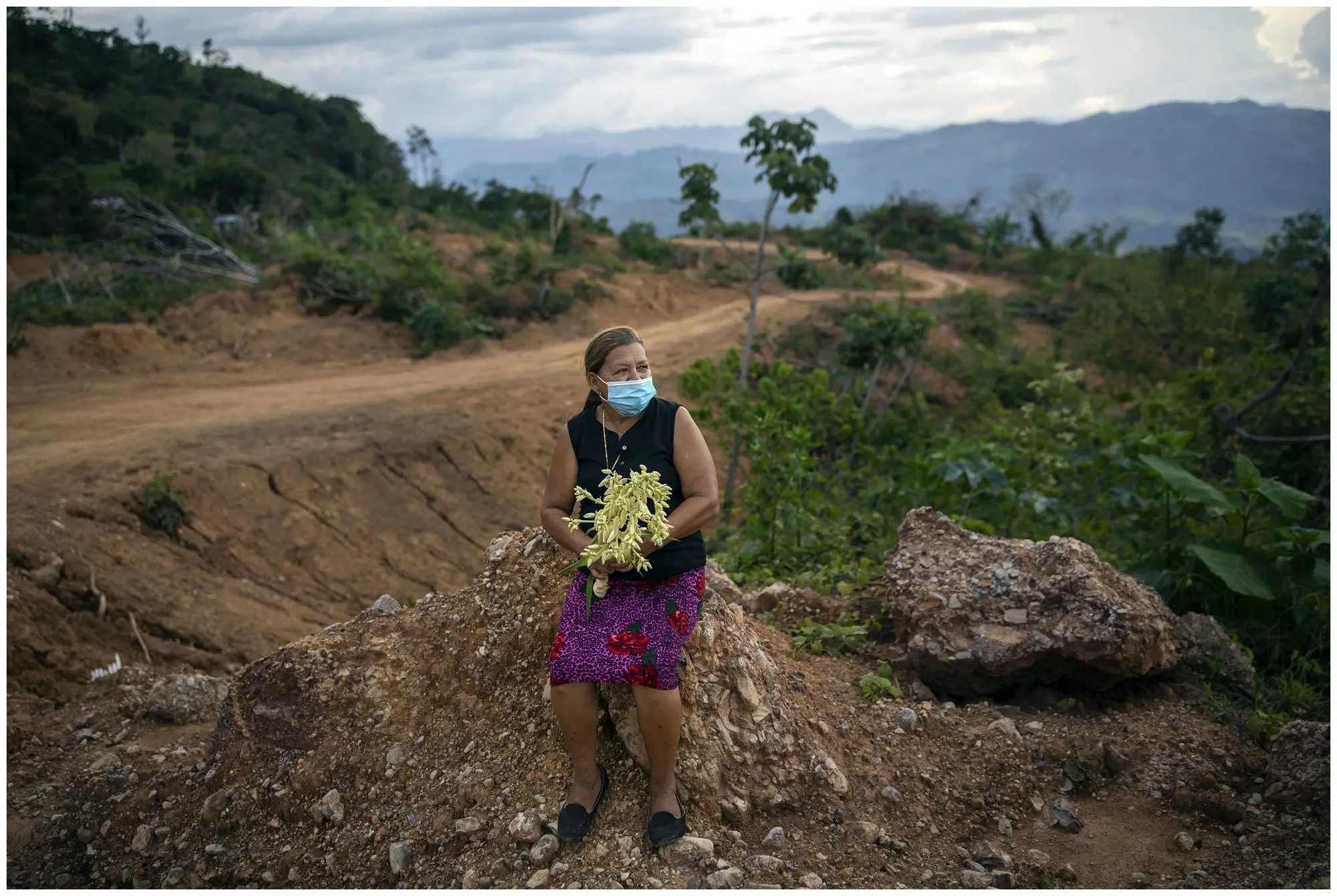 a woman holding a flower on the site where home was destroyed