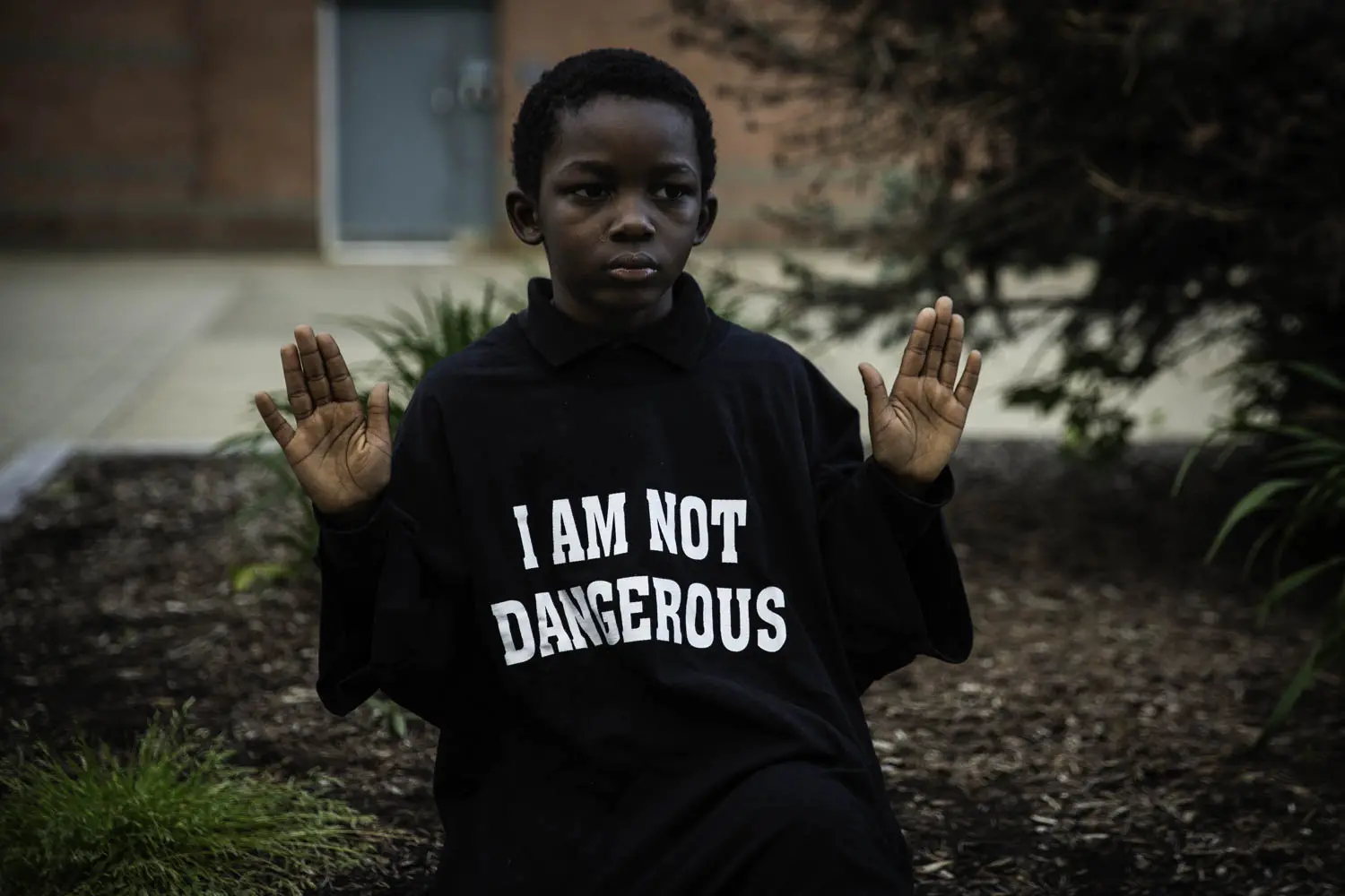 A young boy holds his hands up while wearing a shirt that reads "I am not dangerous."
