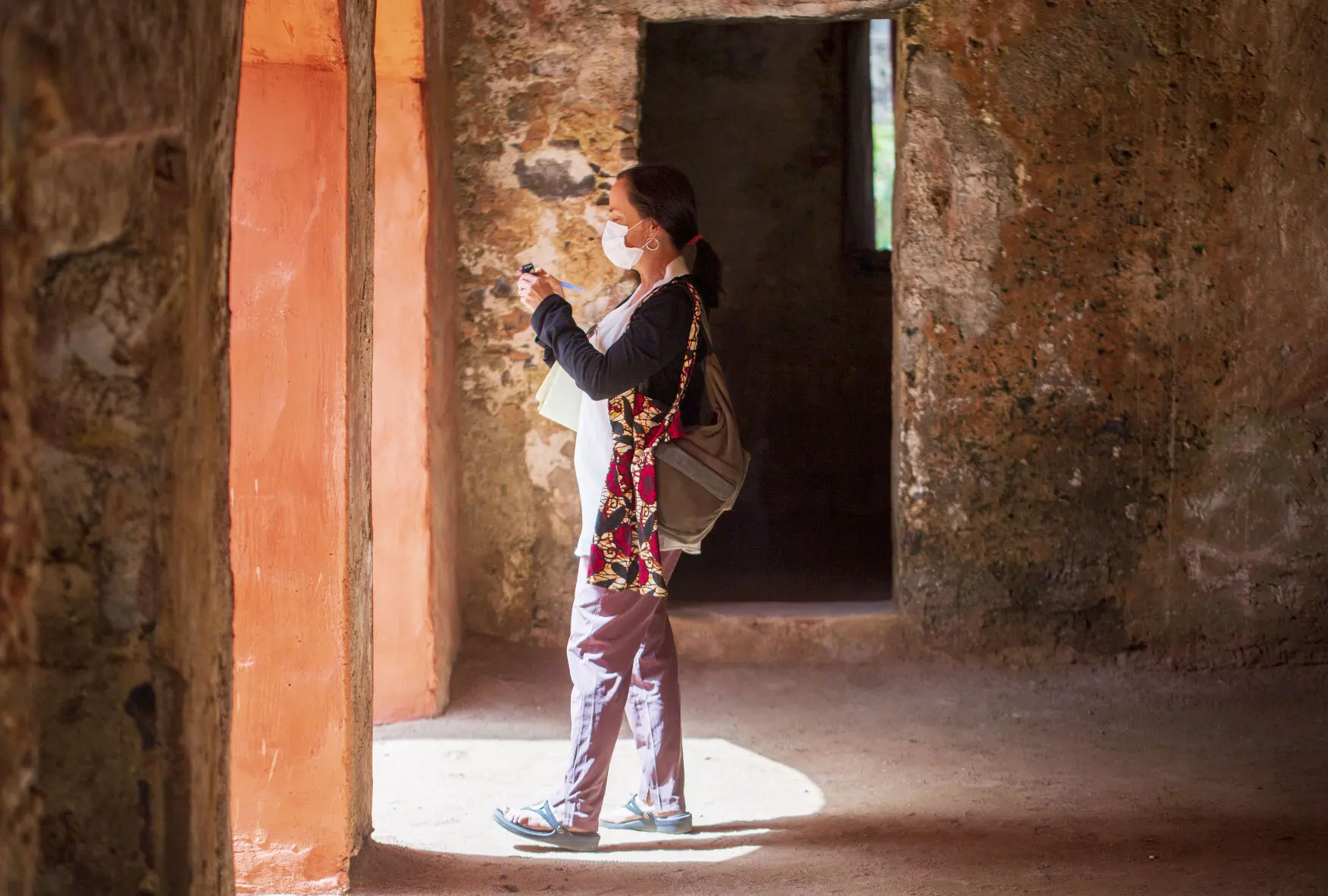 Jennifer Berry Hawes, wearing a medical face mask, stands and takes a photograph in a doorway.