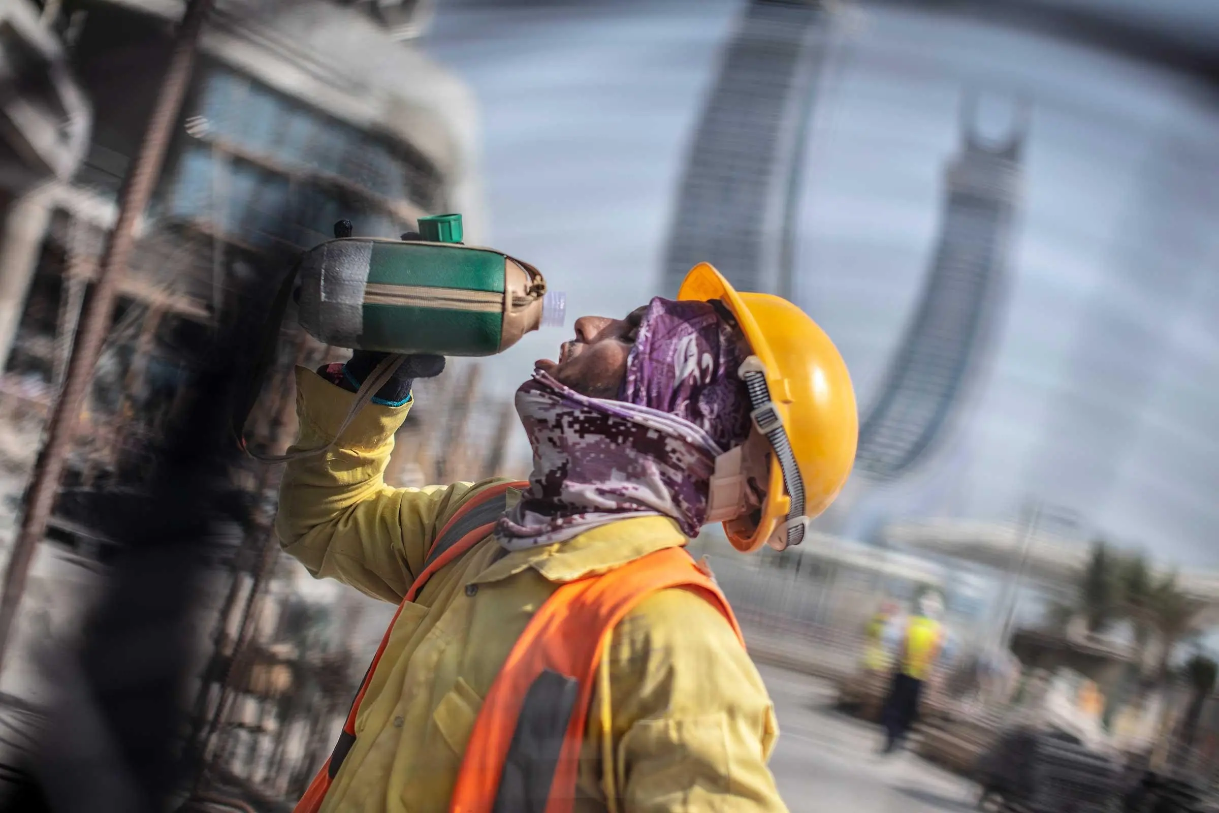 A man in construction gear drinks water from a bottle while working.