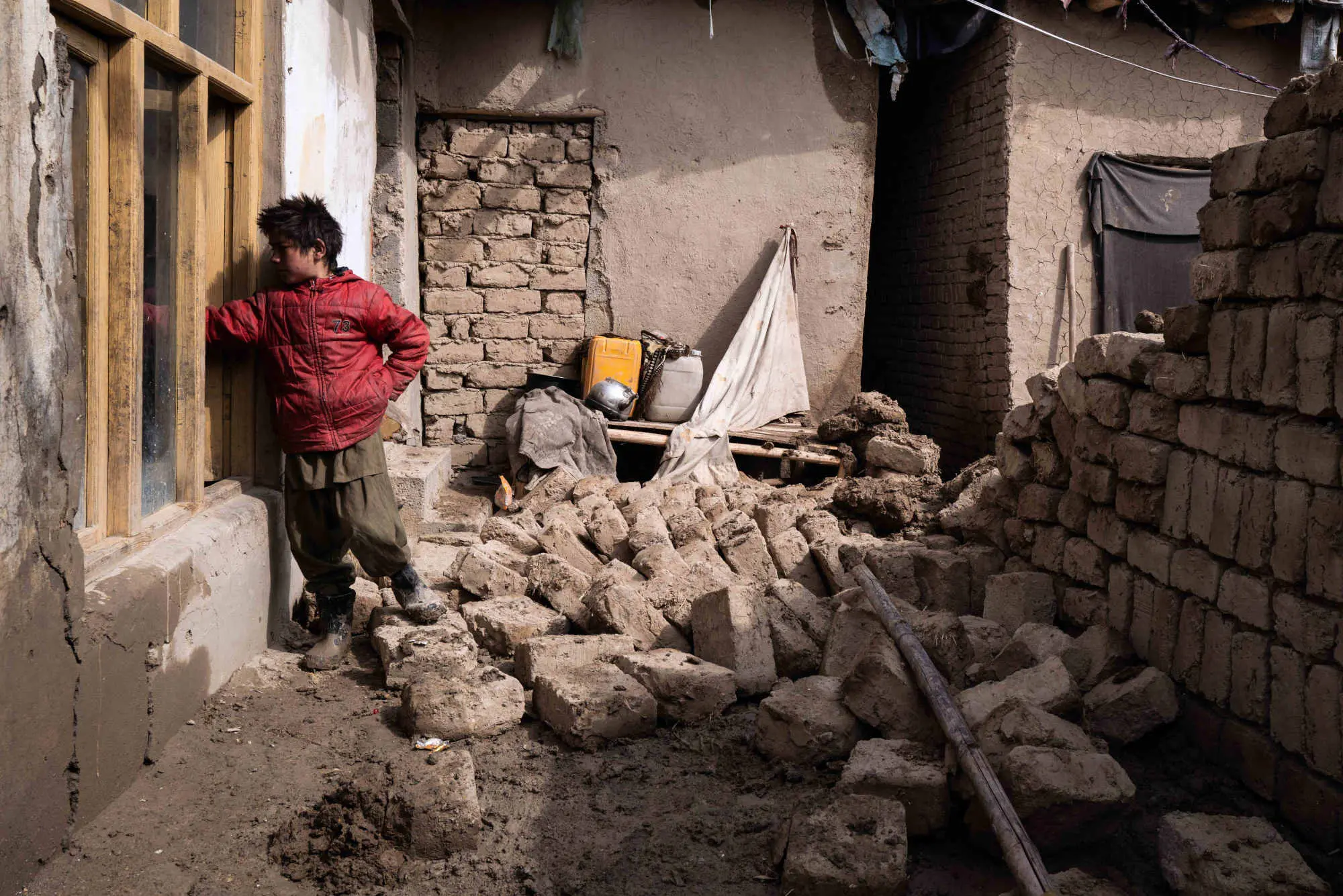 A young boy reaches out through window near collapsed walls