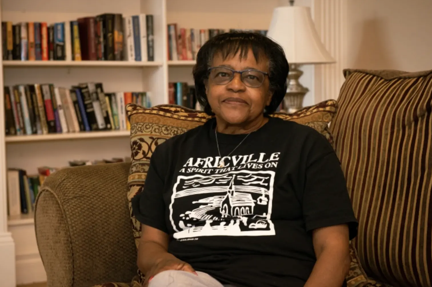 A woman sits in her home, in Africville shirt