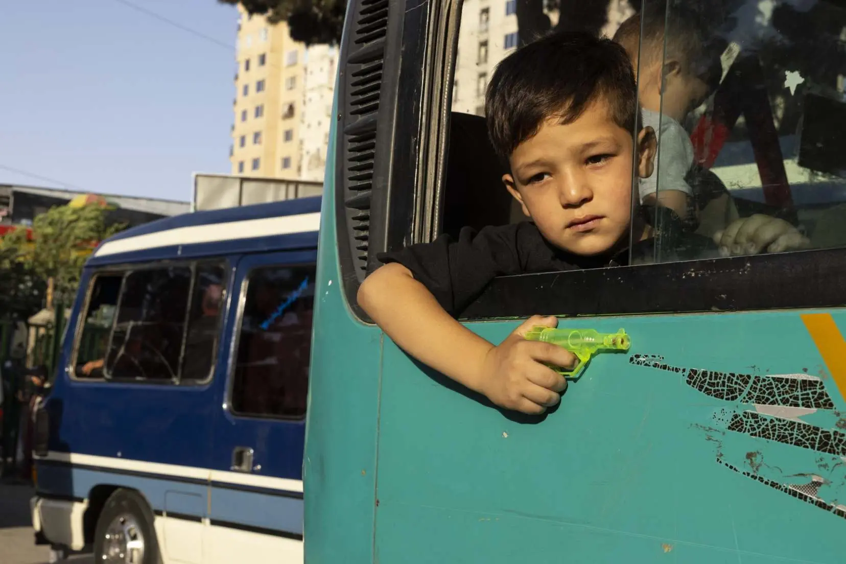 Young boy looks out a window of a car holding a small watergun