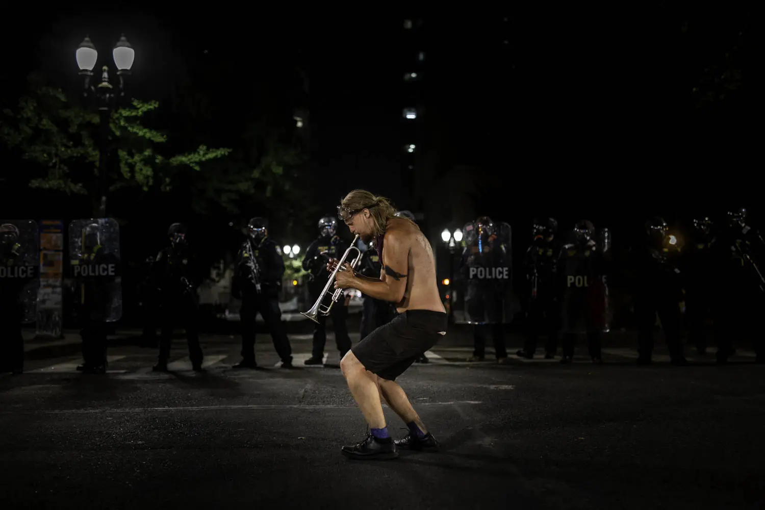 A man plays a trumpet in front of a line of police officers.