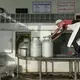 A worker moves cans of fresh milk dropped off by farmers so they can be weighed and tested at Prateep Farms in Pak Chong, Thailand. Image by Mark Hoffman. Thailand, 2019. 