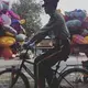 A member of the Chinese military rides his bike past two men selling balloons on Sunday, Sept. 24, 2017, on the same block as the residence of U.S. Ambassador to China Terry Branstad in Beijing, China. Image by Kelsey Kremer. China, 2017.