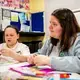 Chloe Crichton, 11, left, cuts out pictures for a vision board during an arts and craft session led by Kelsey Reilly, 19, a Young People's Futures apprentice. Image by Michael Santiago. United Kingdom, 2019.