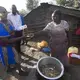 A woman sells a small mixture of chicken intestines and innards and immature eggs wrapped in sheets of used office paper for about 10 cents outside her home in the Korogocho slum. She has been making and selling the mixture for 30 years and was able to help pay for a son to attend a university. Image by Mark Hoffman. Kenya, 2017. 
