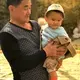 At a park in Beijing, an elderly woman rolls a stroller while this man carries a baby boy. Image by&nbsp;Argentina Maria-Vanderhorst. China, 2018.